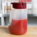 A Tablecraft 32 oz. dispenser jar with a maroon lid filled with red liquid.