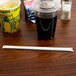 A plastic cup with a straw in it on a table with a brown drink.