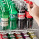 A hand pushes a green plastic soda bottle into a Beverage-Air bottle organizer.