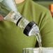 A person using a Choice 3-Ball Measured Liquor Pourer to pour liquid into a glass on a counter.