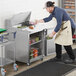 An aproned man uses an Avantco stainless steel cutting top prep table to put food in a container.