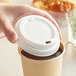 A hand placing a white translucent paper lid on a coffee cup.