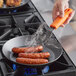 A person uses a Lodge carbon steel fry pan to cook sausages on a stovetop.
