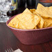 A raspberry polyethylene oval basket filled with tortilla chips on a table in a Mexican restaurant.