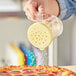 A person using a Choice yellow polycarbonate shaker to sprinkle cheese on a pizza.
