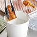 A pair of tongs in a white Innopak bucket of fried chicken.