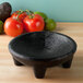 A black HS Inc. polypropylene Molcajete on a wood surface with tomatoes and avocado inside.