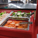 A red Cambro buffet with trays of food in a school kitchen.