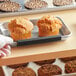 A hand using a Baker's Mark black silicone clip to hold a tray of muffins.