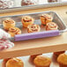 A person using a Baker's Mark purple silicone clip to identify a tray of muffins.