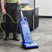 A man using a Clarke CarpetMaster 212 vacuum cleaner with a yellow tube in a corporate office cafeteria.