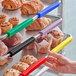 A hand using a green Baker's Mark clip to identify a rack of pastries.