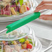 A person using a green Baker's Mark silicone bun pan clip to label a salad container.