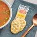 A bowl of tomato soup with a Town House cracker and a spoon on a table.