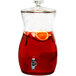 A Stylesetter glass beverage dispenser filled with red liquid and fruit slices.