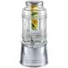 A Stylesetter glass beverage dispenser with fruit inside on a galvanized metal base.