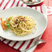 A Tuxton bright white china plate with spaghetti, mushrooms, and carrots.