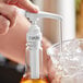 A hand using a white Capora syrup pump to pour liquid into a glass of ice.