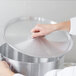 A person's hand holding a silver Vollrath Arkadia stock pot lid.