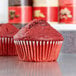 A red cupcake in a Hoffmaster white fluted baking cup.