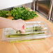 A person cutting asparagus into a clear plastic container with a Cambro 1/3 size FlipLid.