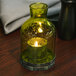 A Sterno green glass lantern liquid candle holder on a table with a lit candle inside.