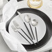 A black plate with Acopa Odin stainless steel flatware on it.