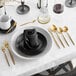 A table setting with a napkin folded on a black plate with gold spoons.