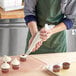 A person in a green apron using an Enjay disposable pastry bag to frost a cupcake.
