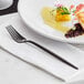 A white plate with food on it and an Acopa Odin black stainless steel dinner fork on the side.