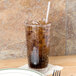 A Cambro clear plastic tumbler filled with soda and ice with a straw.