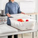 A woman in a chef's uniform holding a white Vigor polyethylene food storage container full of vegetables.