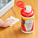 A hand using Sani Professional No-Rinse Sanitizing Wipes to clean a red container on a table.