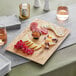 An Acopa faux wood melamine serving board with cheese and grapes on a table.