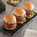 A group of Turano mini brioche slider buns with hamburgers on black plates.