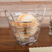 An American Metalcraft round chrome wire basket with handles holding a basket of bread.