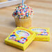 A cupcake with sprinkles and a candle in it on a counter with a yellow box of Sterno multi-colored birthday candles.