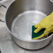 A gloved hand using Arm & Hammer Baking Soda to clean a pot of water.
