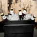 A black American Metalcraft rectangular hammered beverage tub with bottles of beer in ice.