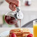 A person pouring syrup from a Choice Glass Teardrop Syrup Dispenser onto a plate of french toast.