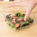 A hand holding a Sabert clear plastic square bowl filled with salad.