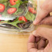 A person using a Sabert clear plastic container to hold salad while cutting it.