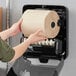 A person holding a roll of Tork Universal Matic Natural Kraft paper towels in front of a dispenser.