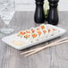 A rectangular white porcelain china tray with sushi rolls on a wood table.