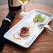 A rectangular white porcelain china tray on a table with a scallop and wine.
