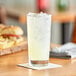 A glass of Tropicana lemonade on a table with a coaster.