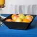A black Siciliano square bowl filled with oranges on a table.