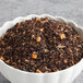 A bowl of brown and black Davidson's Organic Decaf Cinnamon Apple Loose Leaf Tea leaves with dried oranges.