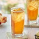 A glass of Davidson's Organic Decaf Tropical Iced Tea with ice cubes and a basket of croissants on a table.