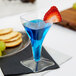 A clear plastic square wine glass filled with blue liquid and a strawberry on top.